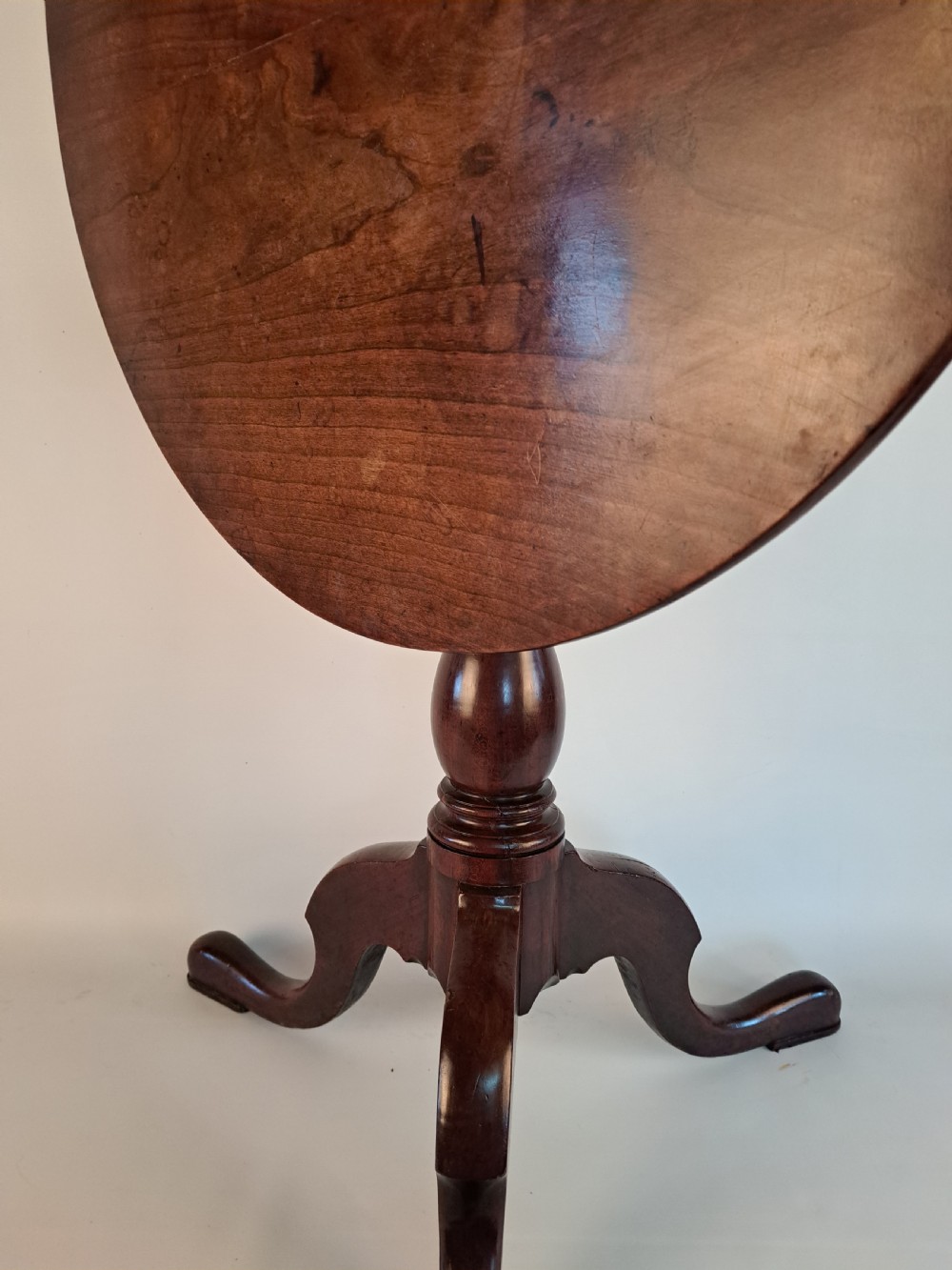 A Georgian mahogany tilt-top table with a circular timber top tilted vertically above a vase-turned pedestal stem and three cabriole legs. View XXVIII