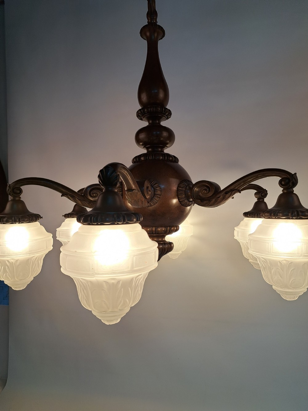 A five-arm dark bronze chandelier featuring a central turned stem, curved scroll arms, and downward-facing frosted glass shades. View IV