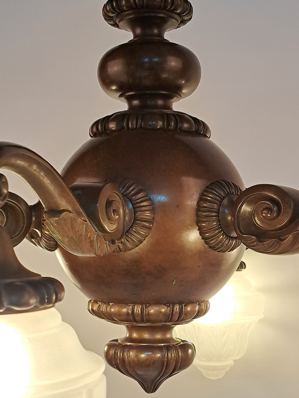 A five-arm dark bronze chandelier featuring a central turned stem, curved scroll arms, and downward-facing frosted glass shades. View VI