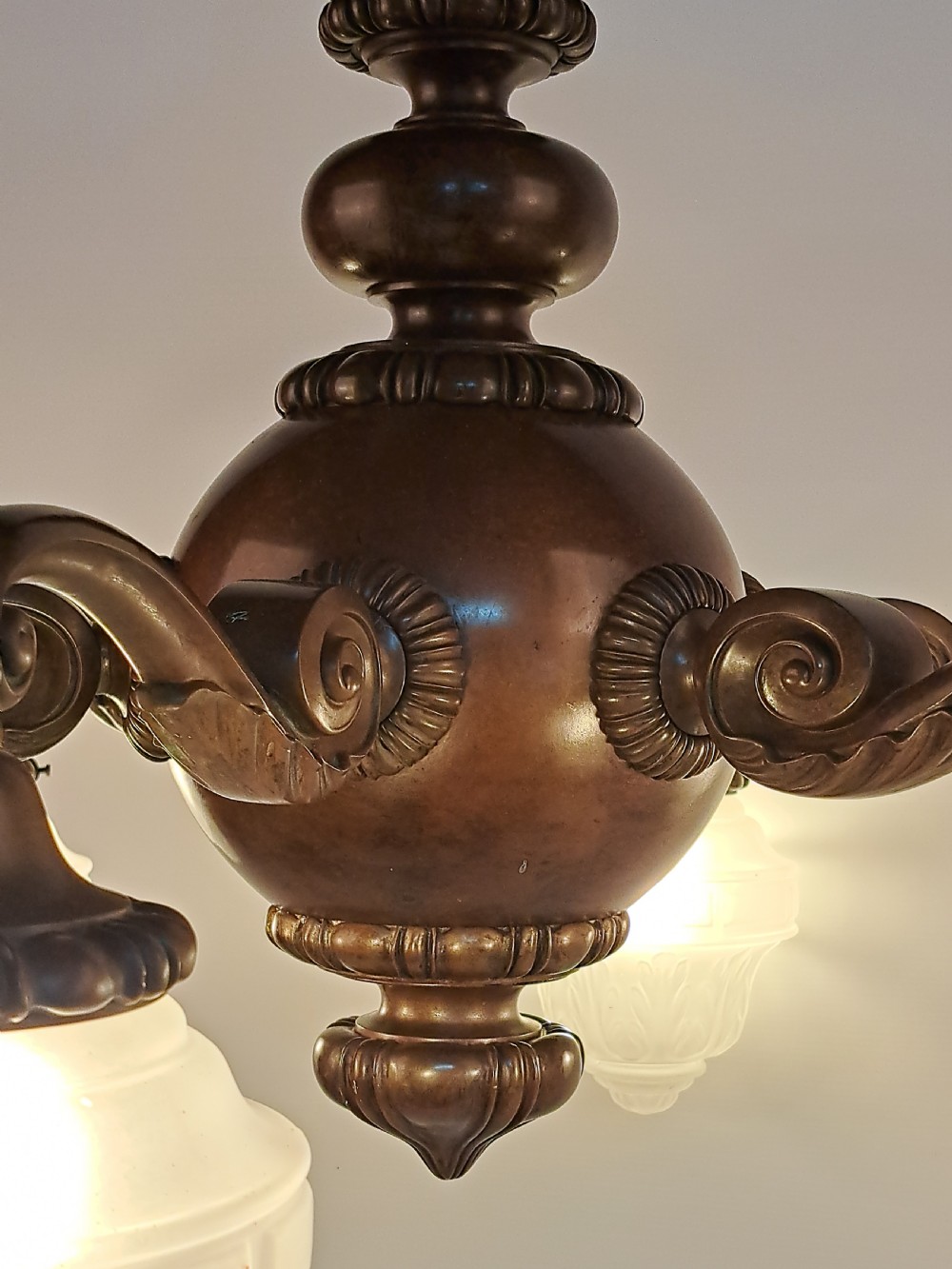 A five-arm dark bronze chandelier featuring a central turned stem, curved scroll arms, and downward-facing frosted glass shades. View VII