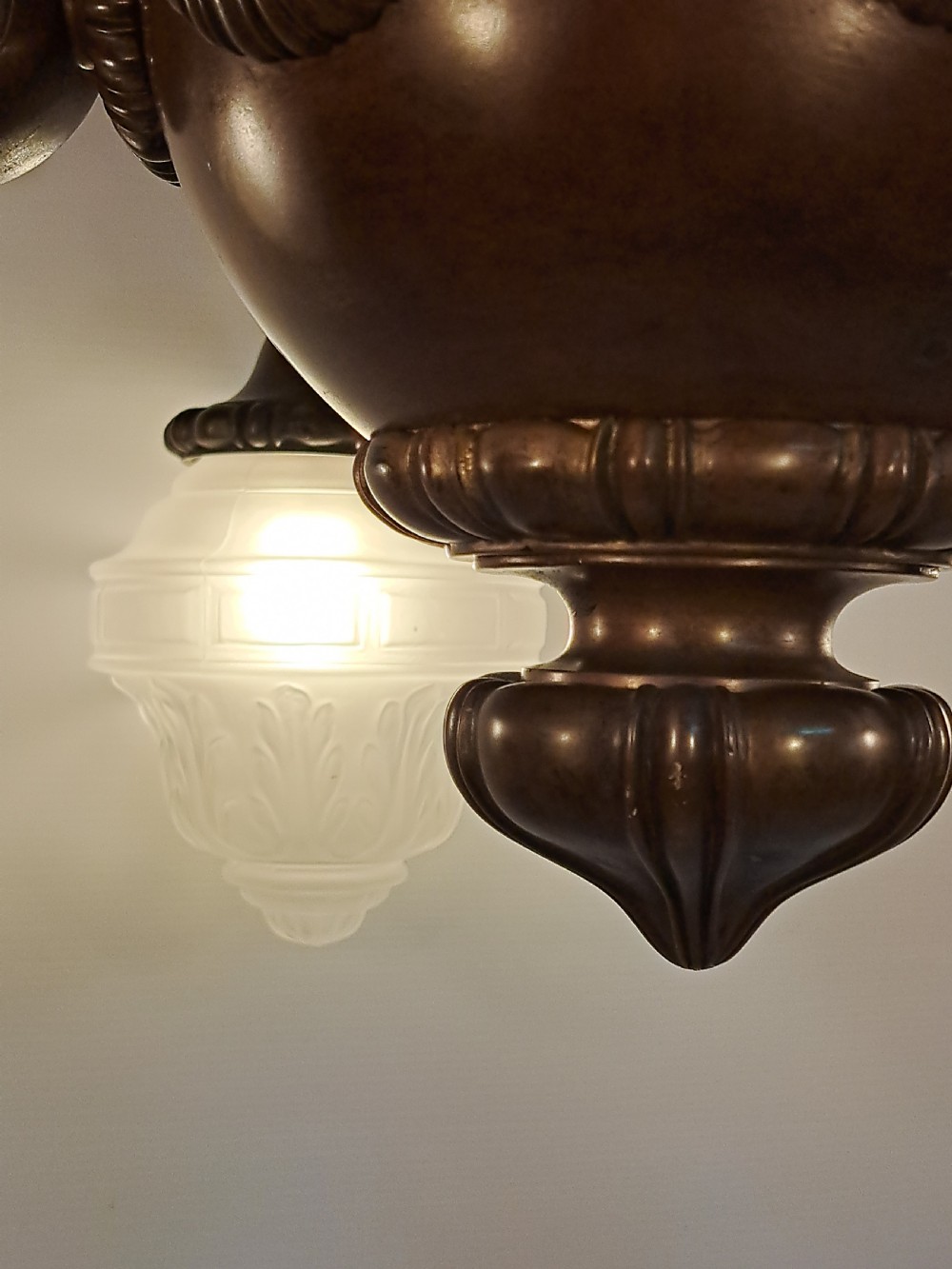 A five-arm dark bronze chandelier featuring a central turned stem, curved scroll arms, and downward-facing frosted glass shades. View XII
