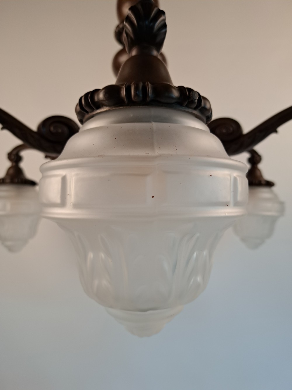 A five-arm dark bronze chandelier featuring a central turned stem, curved scroll arms, and downward-facing frosted glass shades. View XXII