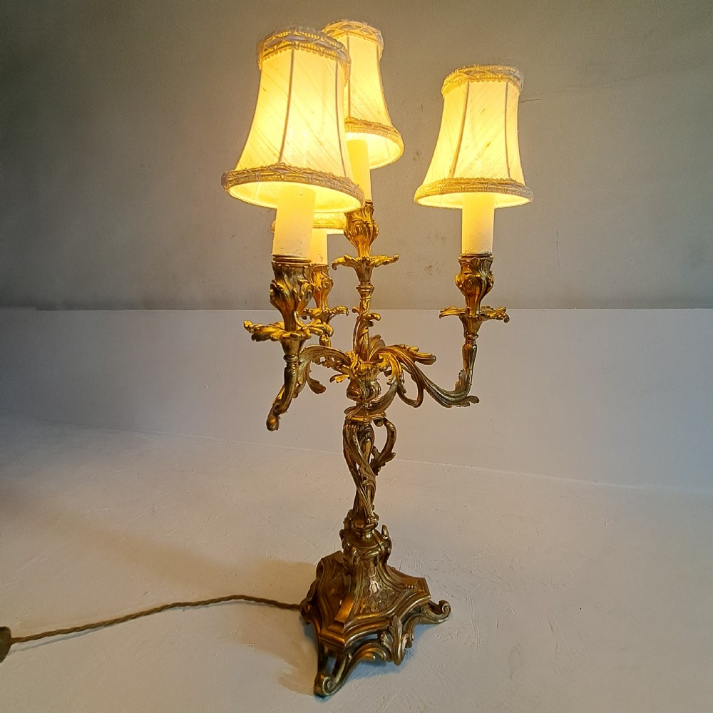 An ornate four-light gilt bronze candelabra table lamp in Rococo Revival style with flared fabric shades and cast scrollwork.