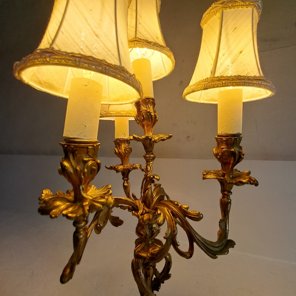 An ornate four-light gilt bronze candelabra table lamp in Rococo Revival style with flared fabric shades and cast scrollwork. View X