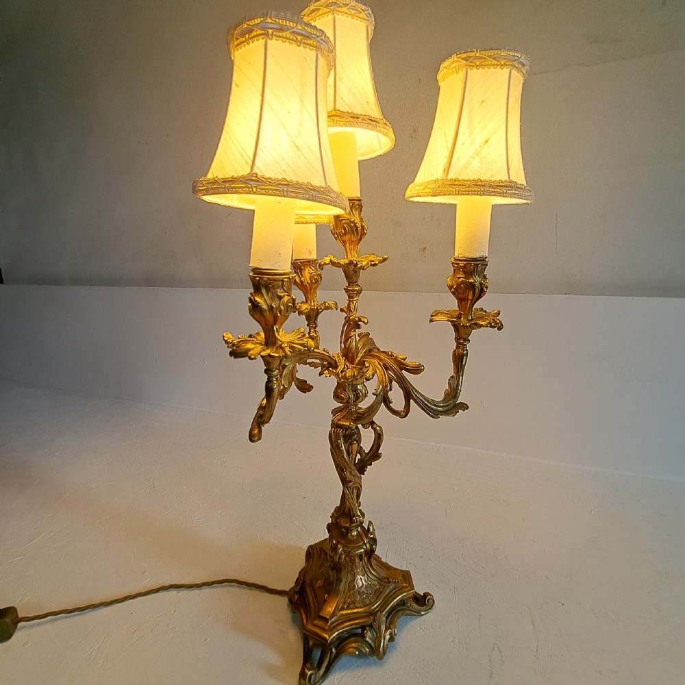 An ornate four-light gilt bronze candelabra table lamp in Rococo Revival style with flared fabric shades and cast scrollwork. View XI