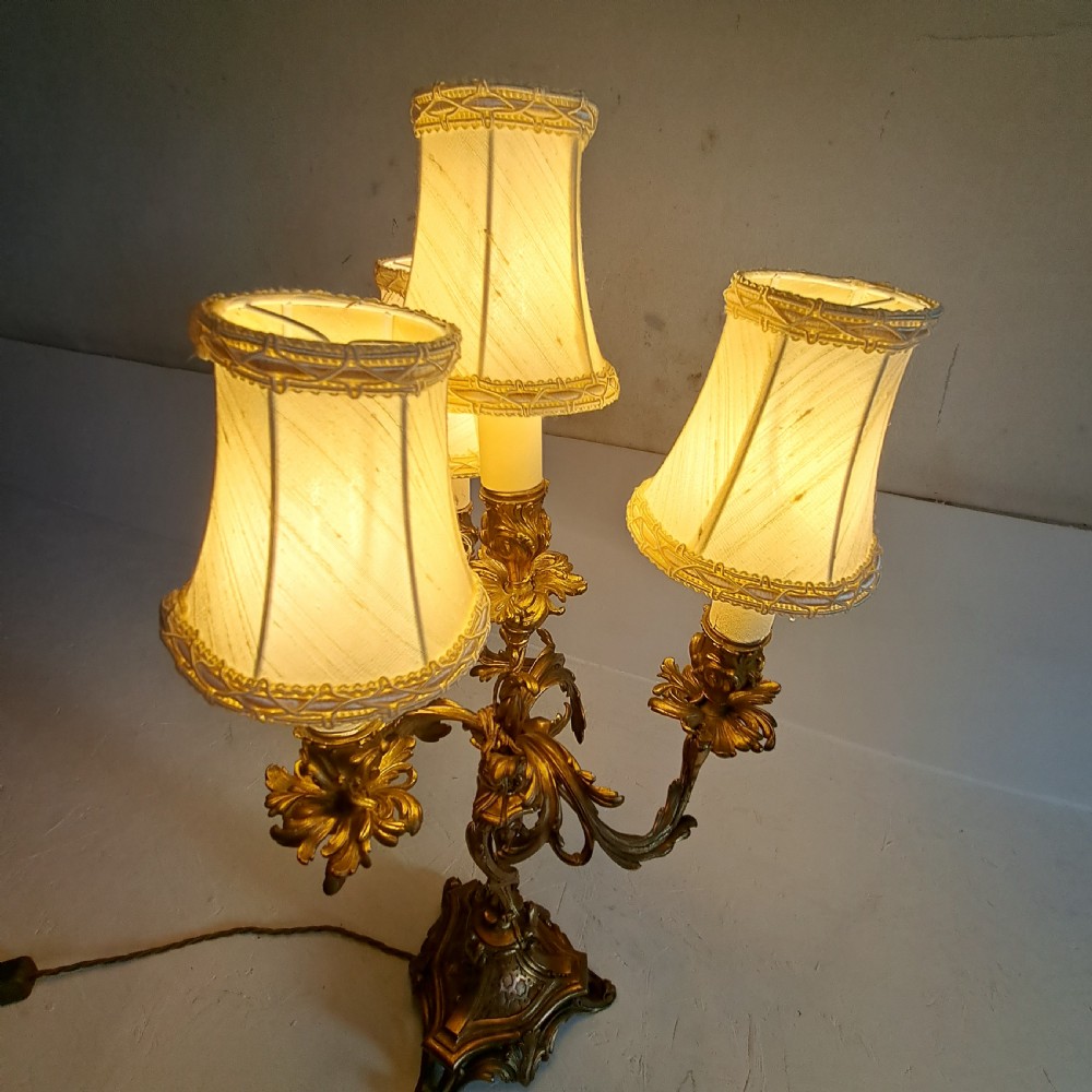 An ornate four-light gilt bronze candelabra table lamp in Rococo Revival style with flared fabric shades and cast scrollwork. View XII