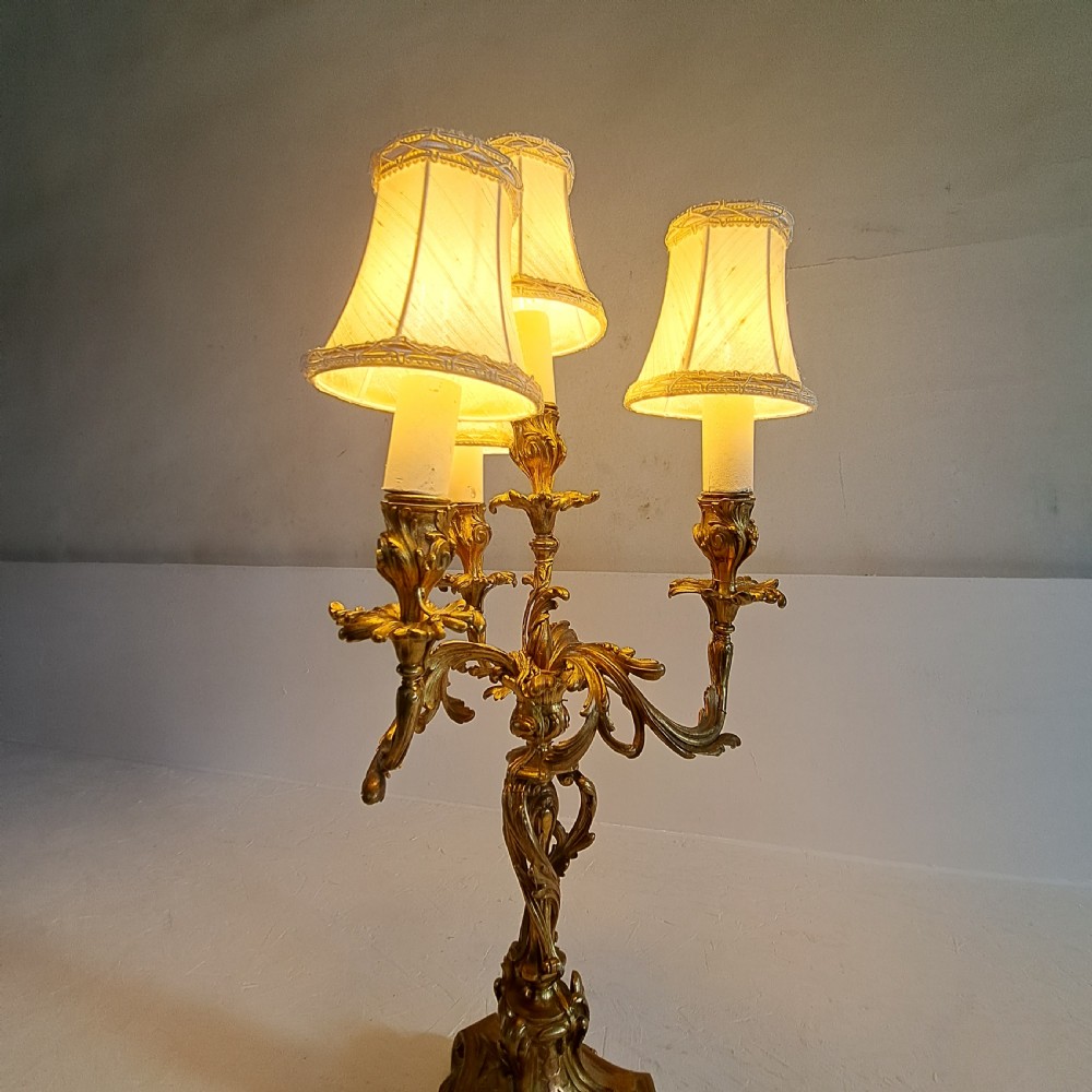 An ornate four-light gilt bronze candelabra table lamp in Rococo Revival style with flared fabric shades and cast scrollwork. View XVI