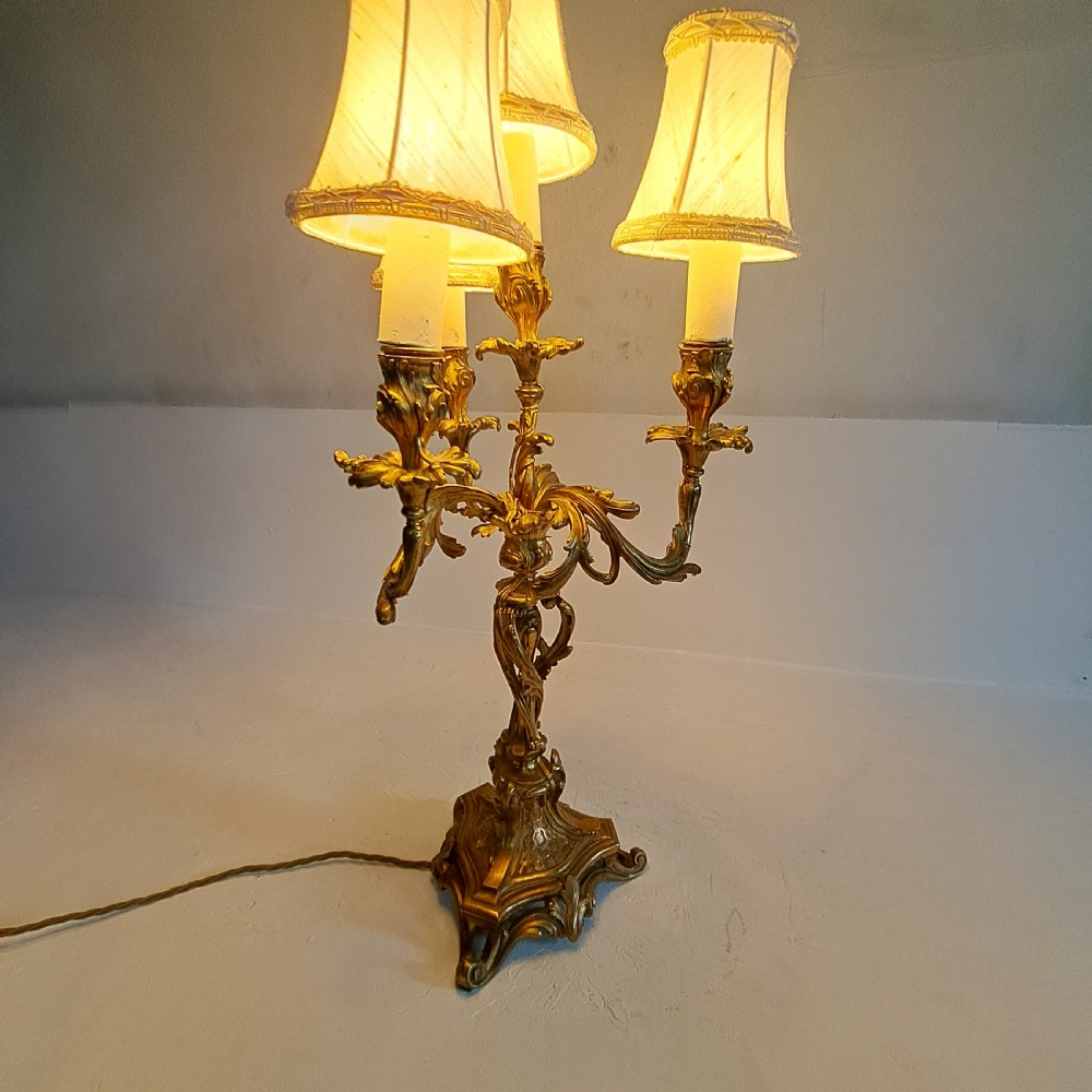 An ornate four-light gilt bronze candelabra table lamp in Rococo Revival style with flared fabric shades and cast scrollwork. View XVII
