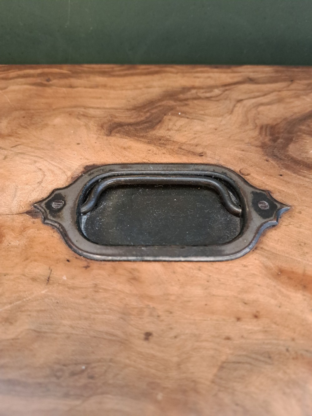 A rectangular blonde walnut jewellery box with a brass keyhole escutcheon and recessed handle on the lid, resting on a dark marble surface. View II