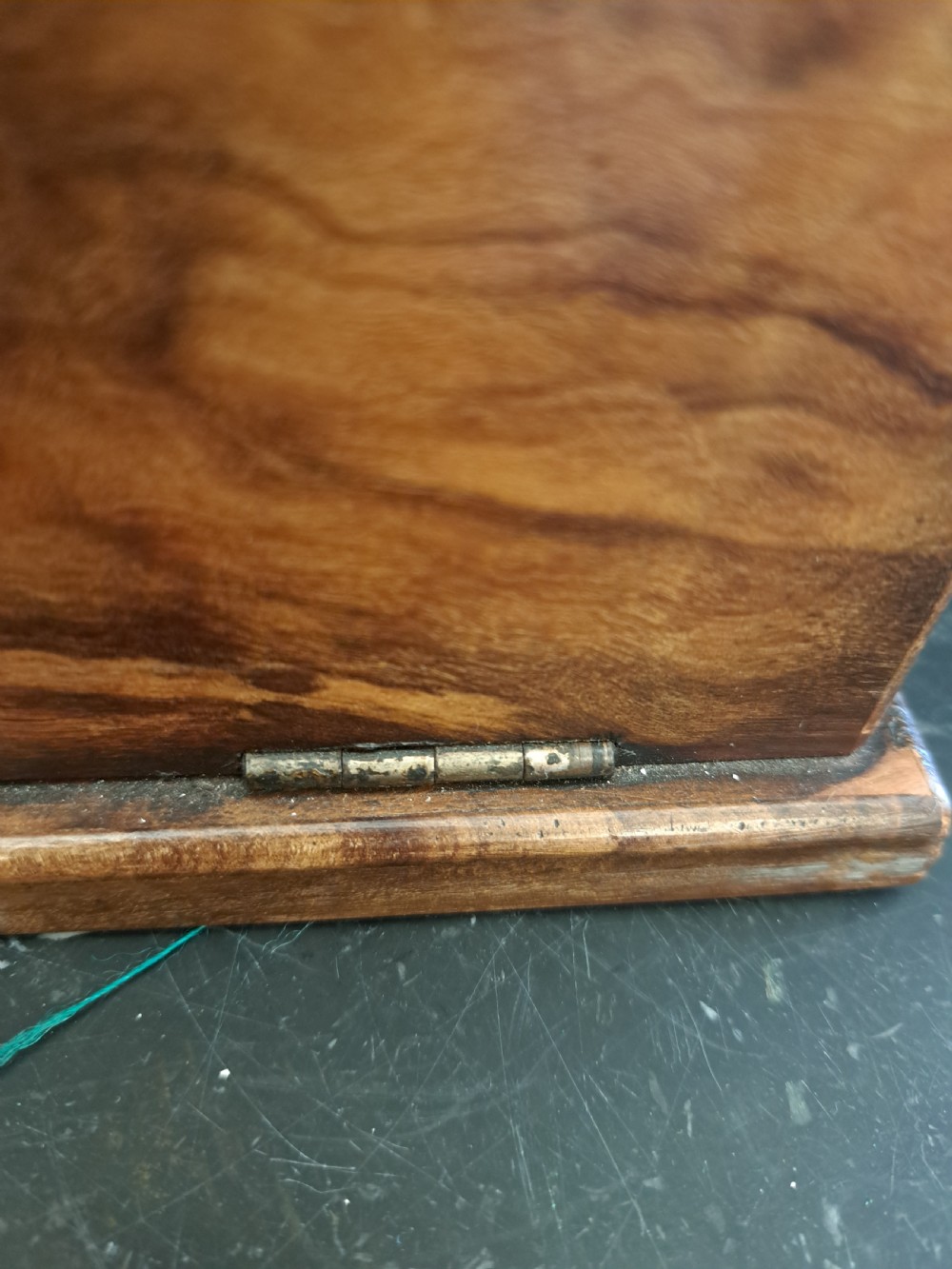 A rectangular blonde walnut jewellery box with a brass keyhole escutcheon and recessed handle on the lid, resting on a dark marble surface. View VI