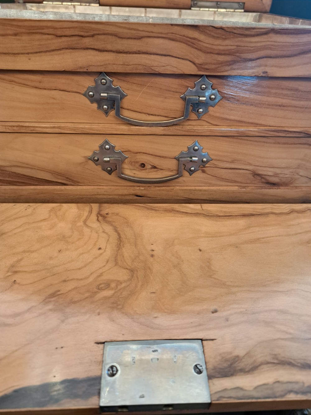 A rectangular blonde walnut jewellery box with a brass keyhole escutcheon and recessed handle on the lid, resting on a dark marble surface. View VIII