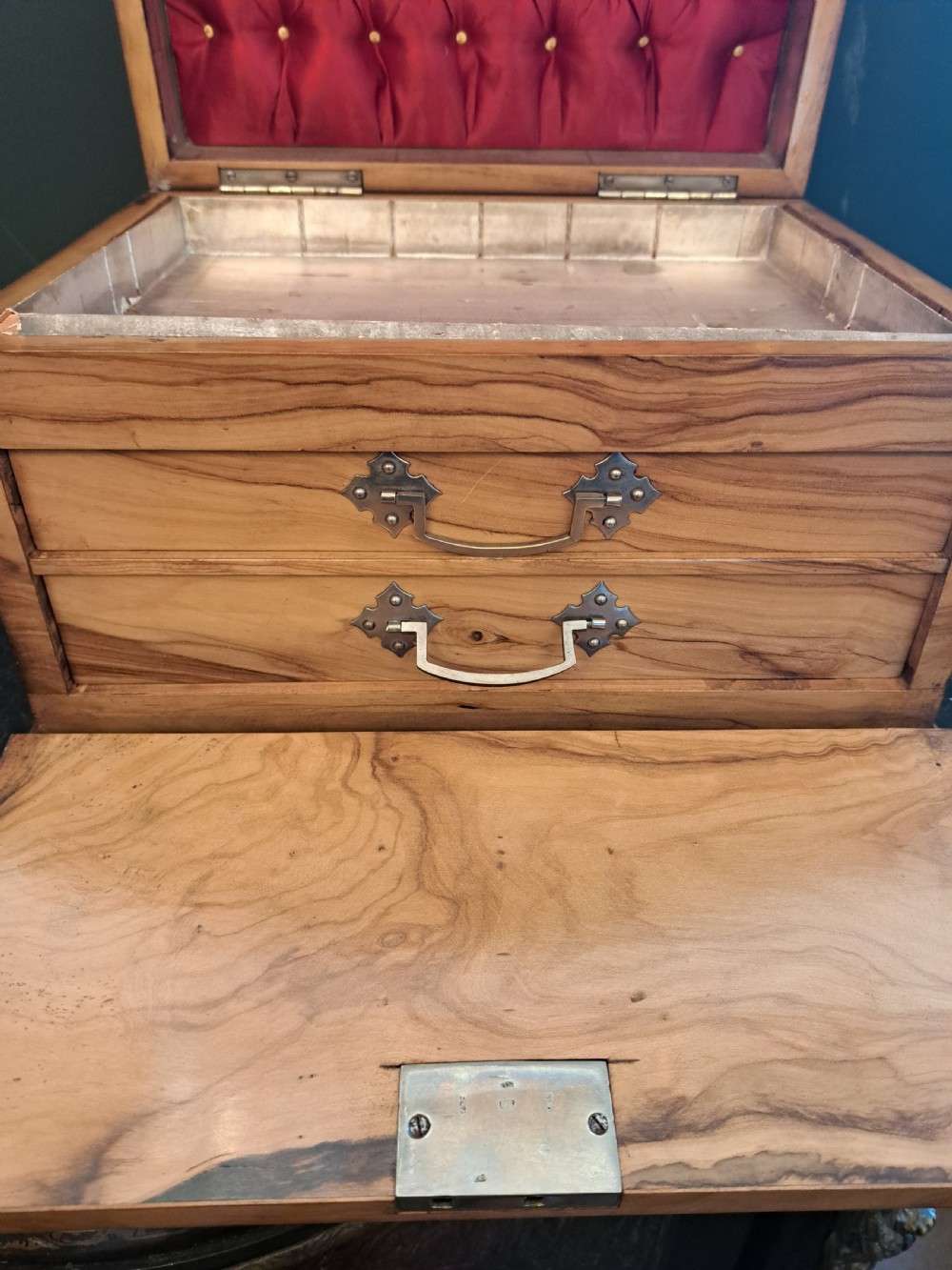 A rectangular blonde walnut jewellery box with a brass keyhole escutcheon and recessed handle on the lid, resting on a dark marble surface. View IX