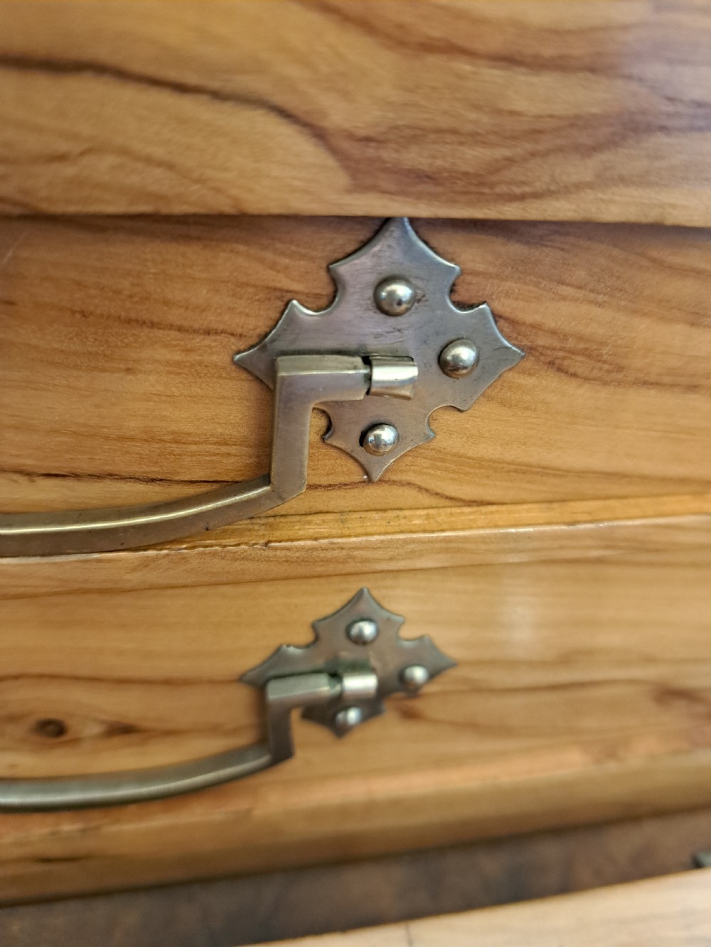 A rectangular blonde walnut jewellery box with a brass keyhole escutcheon and recessed handle on the lid, resting on a dark marble surface. View X