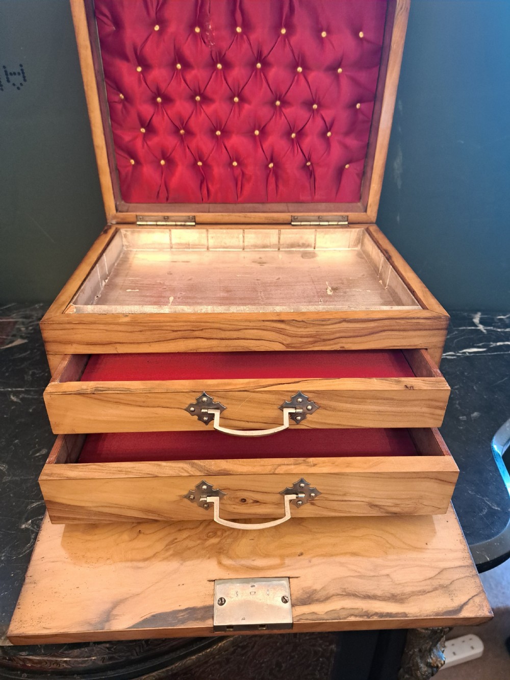 A rectangular blonde walnut jewellery box with a brass keyhole escutcheon and recessed handle on the lid, resting on a dark marble surface. View XVII