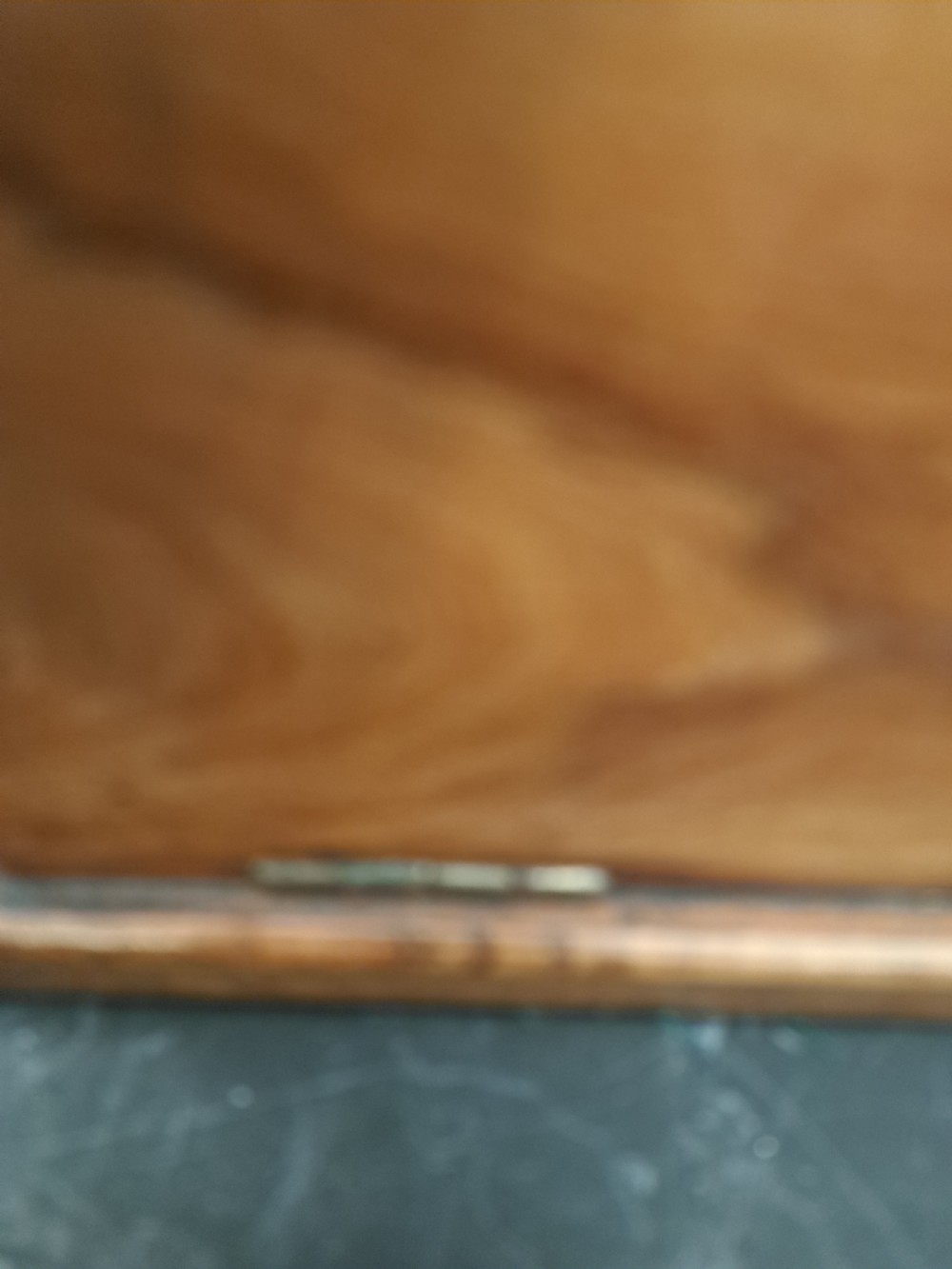 A rectangular blonde walnut jewellery box with a brass keyhole escutcheon and recessed handle on the lid, resting on a dark marble surface. View XVIII
