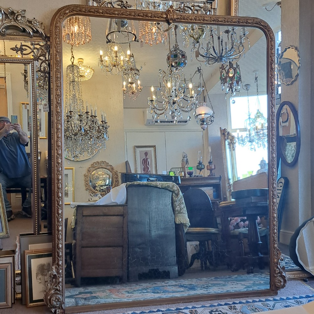 A large rectangular Georgian overmantel mirror featuring a rounded upper frame with gilded bead moulding and decorative foliate corner scrolls.