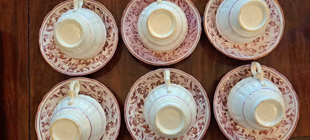 A set of six antique pink lustreware teacups with matching saucers featuring hand-painted botanical foliage patterns on a cream ceramic background. View XII