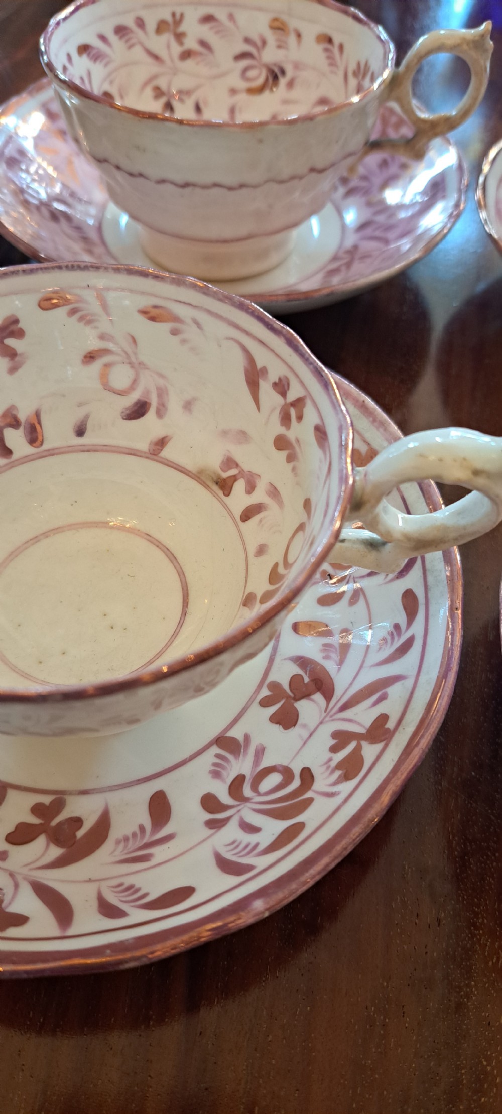 A set of six antique pink lustreware teacups with matching saucers featuring hand-painted botanical foliage patterns on a cream ceramic background. View VIII