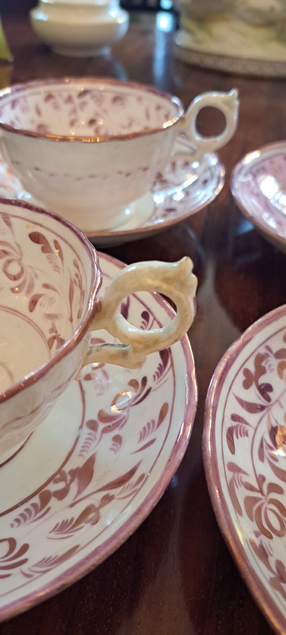 A set of six antique pink lustreware teacups with matching saucers featuring hand-painted botanical foliage patterns on a cream ceramic background. View IX