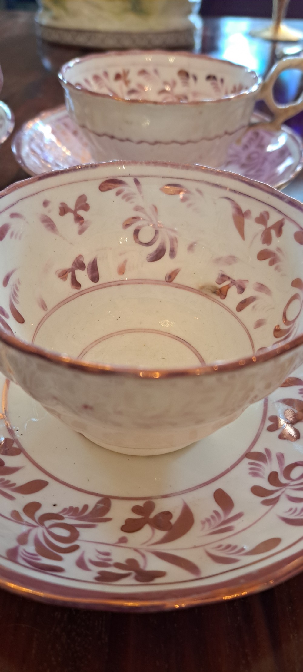 A set of six antique pink lustreware teacups with matching saucers featuring hand-painted botanical foliage patterns on a cream ceramic background. View X
