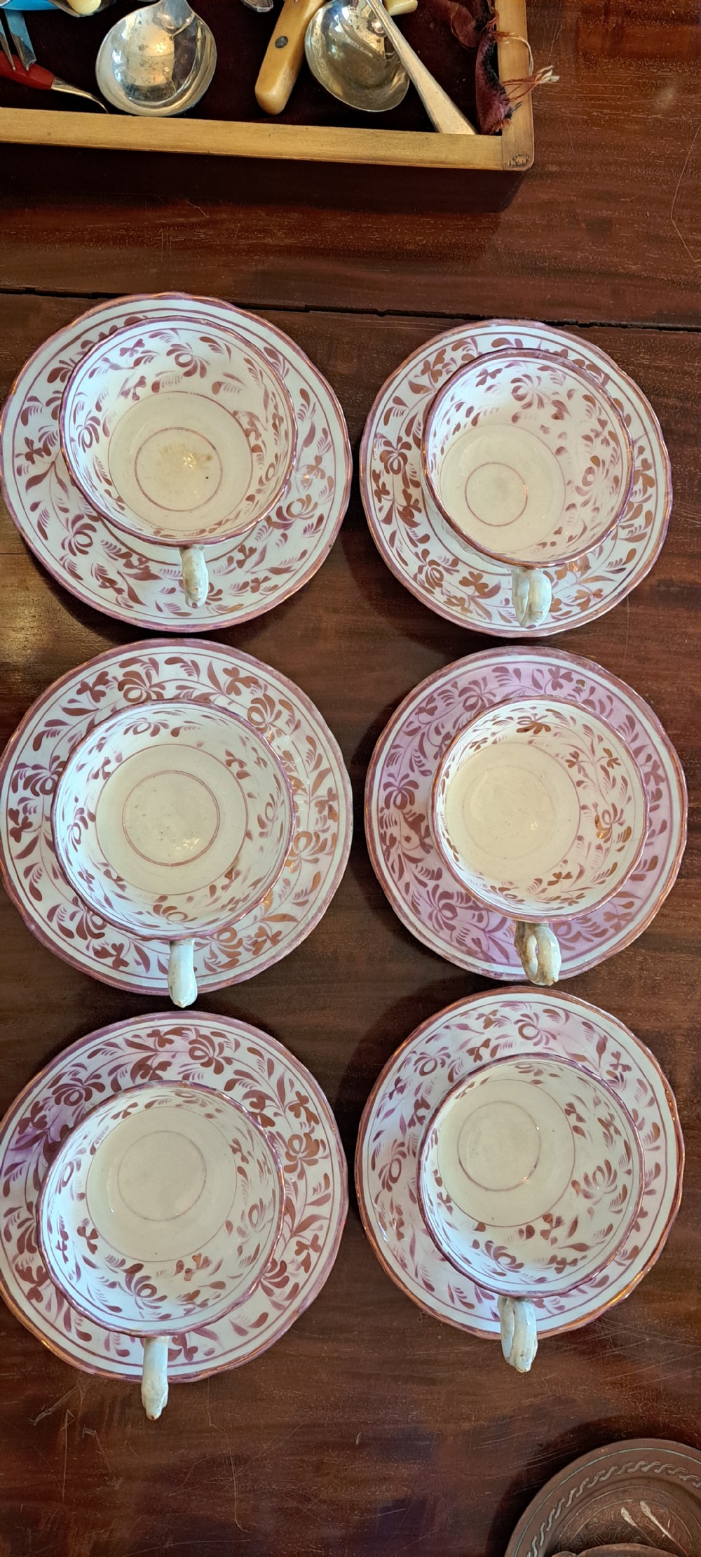 A set of six antique pink lustreware teacups with matching saucers featuring hand-painted botanical foliage patterns on a cream ceramic background.