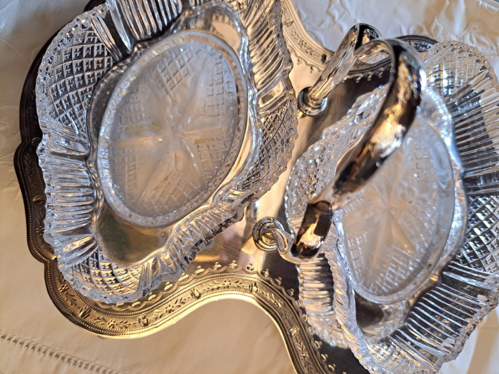 An Edwardian silver-plated relish caddy featuring a central carrying handle and two fitted cut-glass dishes with geometric patterns.