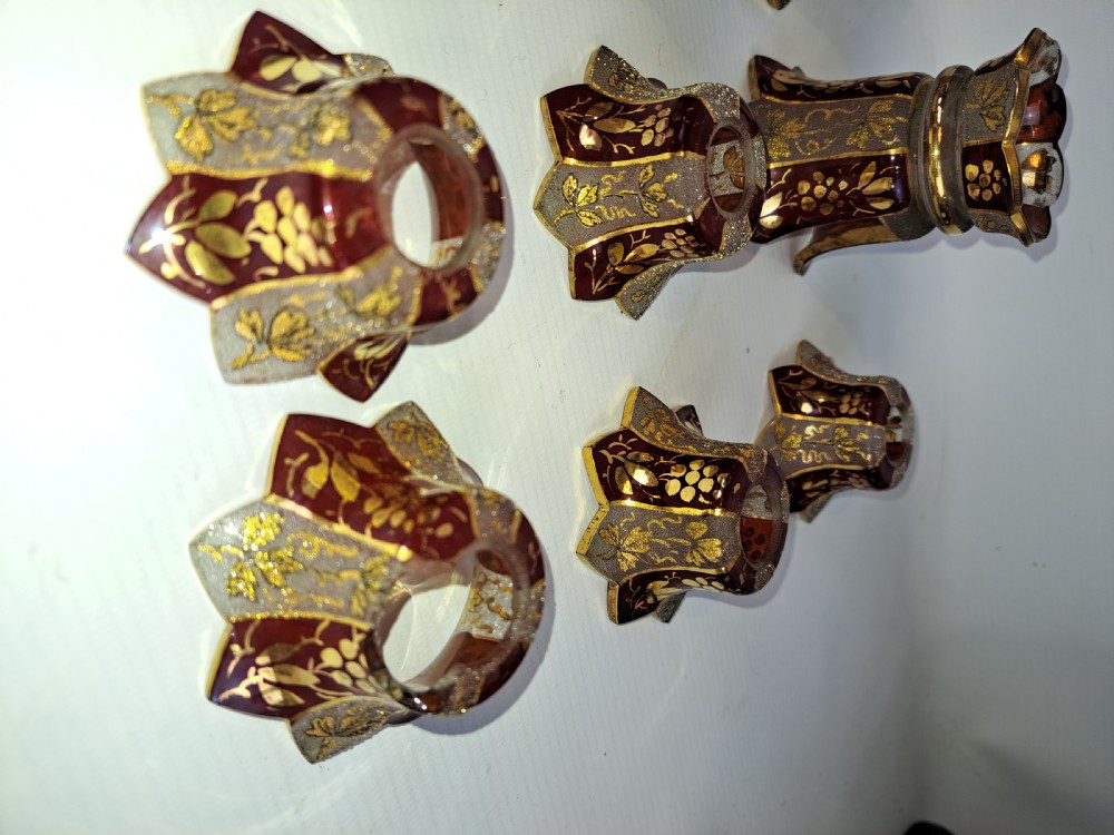 An assortment of ruby stained glass candle nozzles and capitals featuring etched floral motifs and scalloped gilded borders. View II