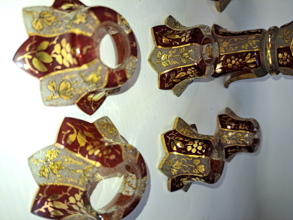 An assortment of ruby stained glass candle nozzles and capitals featuring etched floral motifs and scalloped gilded borders. View V