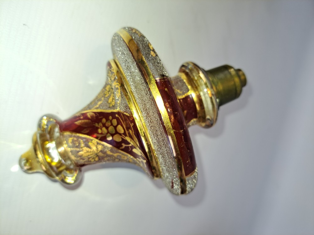 An antique Bohemian ruby glass finial featuring gold leaf floral etching, frosted glass texturing, and a brass threaded mount.