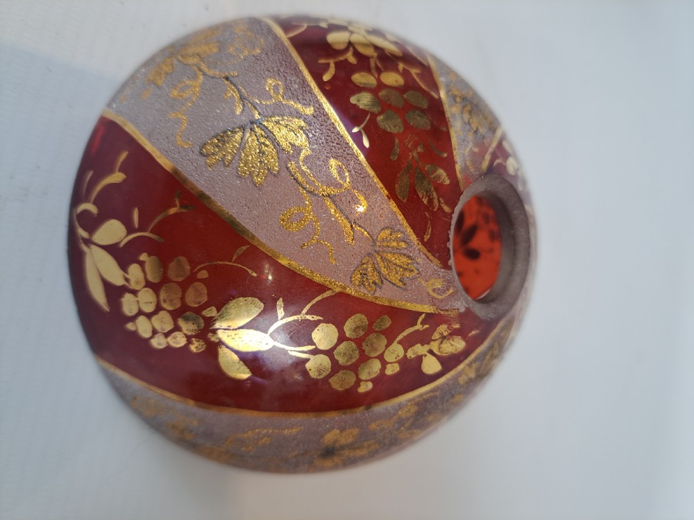A hemispherical ruby red glass chandelier bowl featuring frosted diagonal panels, gilded grapevine motifs, and a central circular hole.
