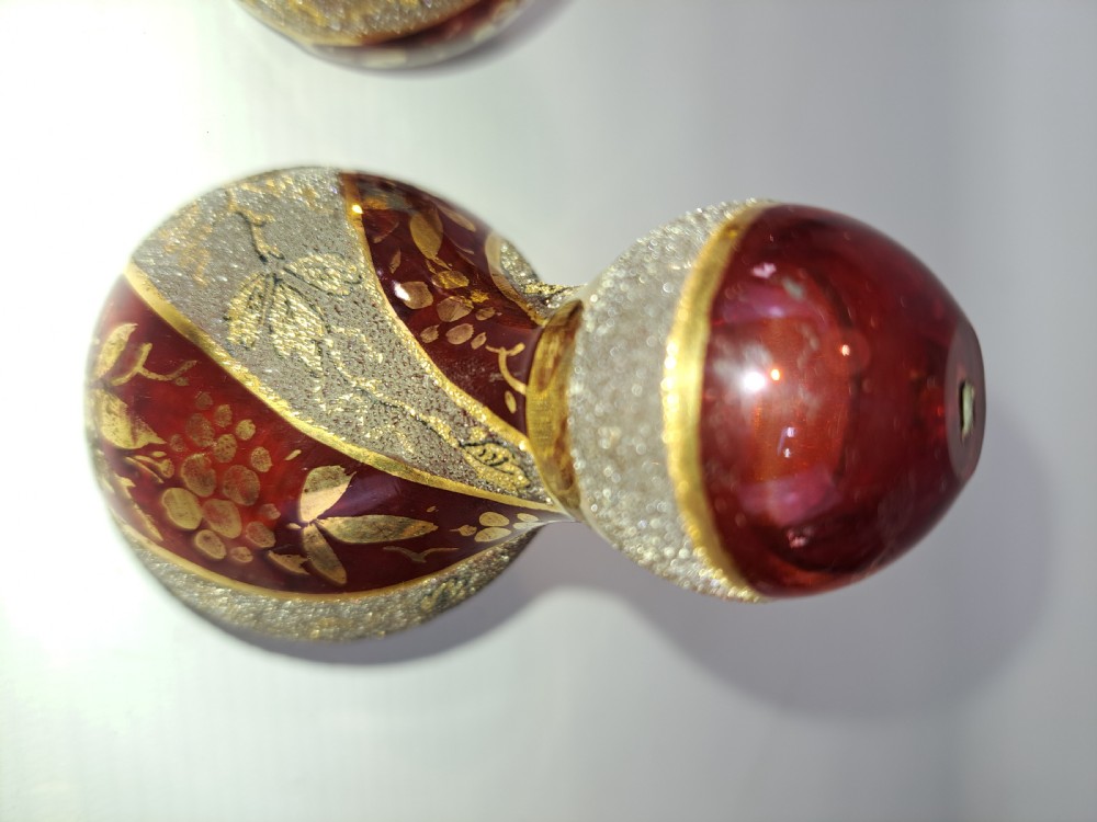 A pair of ruby red glass decorative bells featuring hand-painted gold foliage motifs and textured gilded bands. View IV