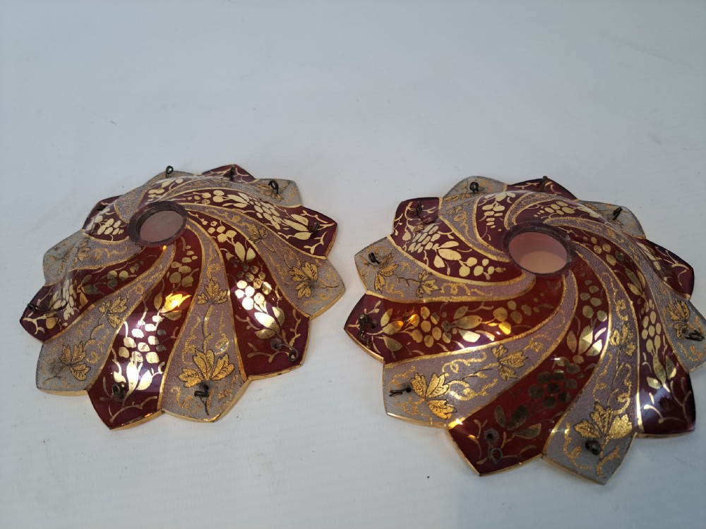 A pair of scalloped Bohemian ruby glass bobeches with frosted panels, hand-painted gold leaf vine patterns, and small metal wire loops.