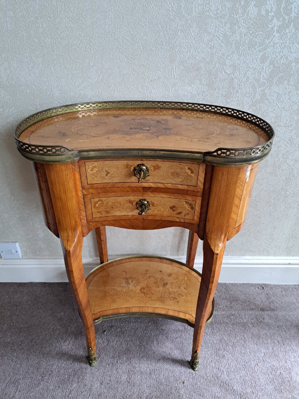A kidney-shaped French marquetry side table featuring floral timber inlays, two drawers, a pierced brass gallery top, and a lower shelf.