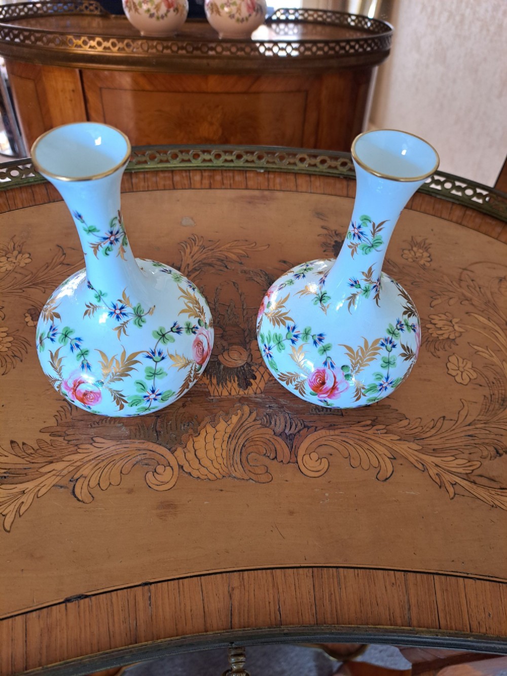A pair of white porcelain bud vases featuring hand-painted floral motifs in pink, blue, and green with gilded rims and leaf accents.