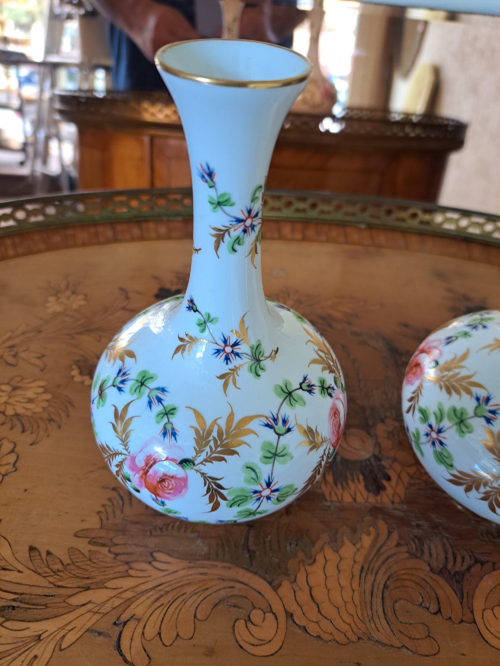 A pair of white porcelain bud vases featuring hand-painted floral motifs in pink, blue, and green with gilded rims and leaf accents. View II