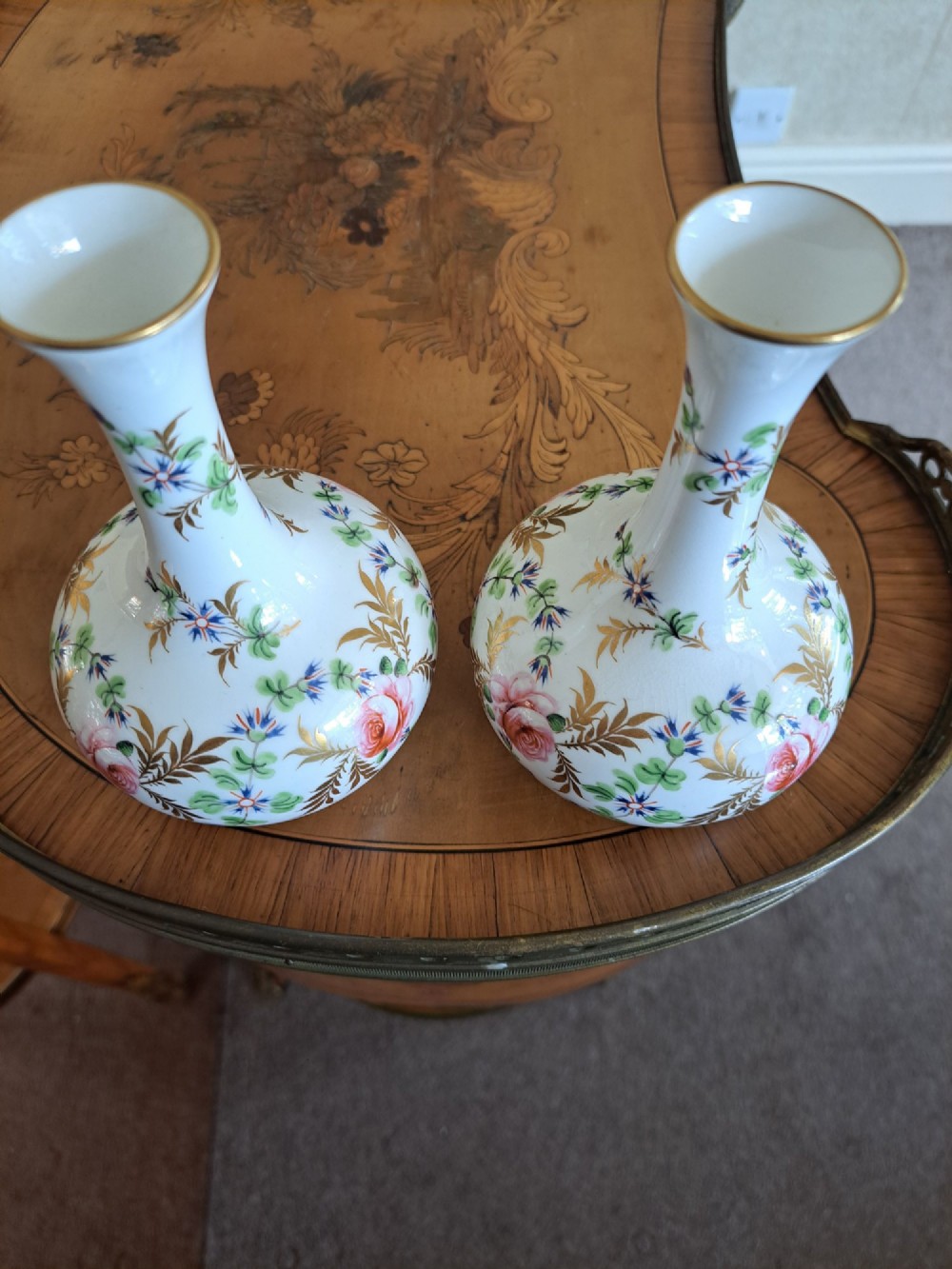 A pair of white porcelain bud vases featuring hand-painted floral motifs in pink, blue, and green with gilded rims and leaf accents. View X