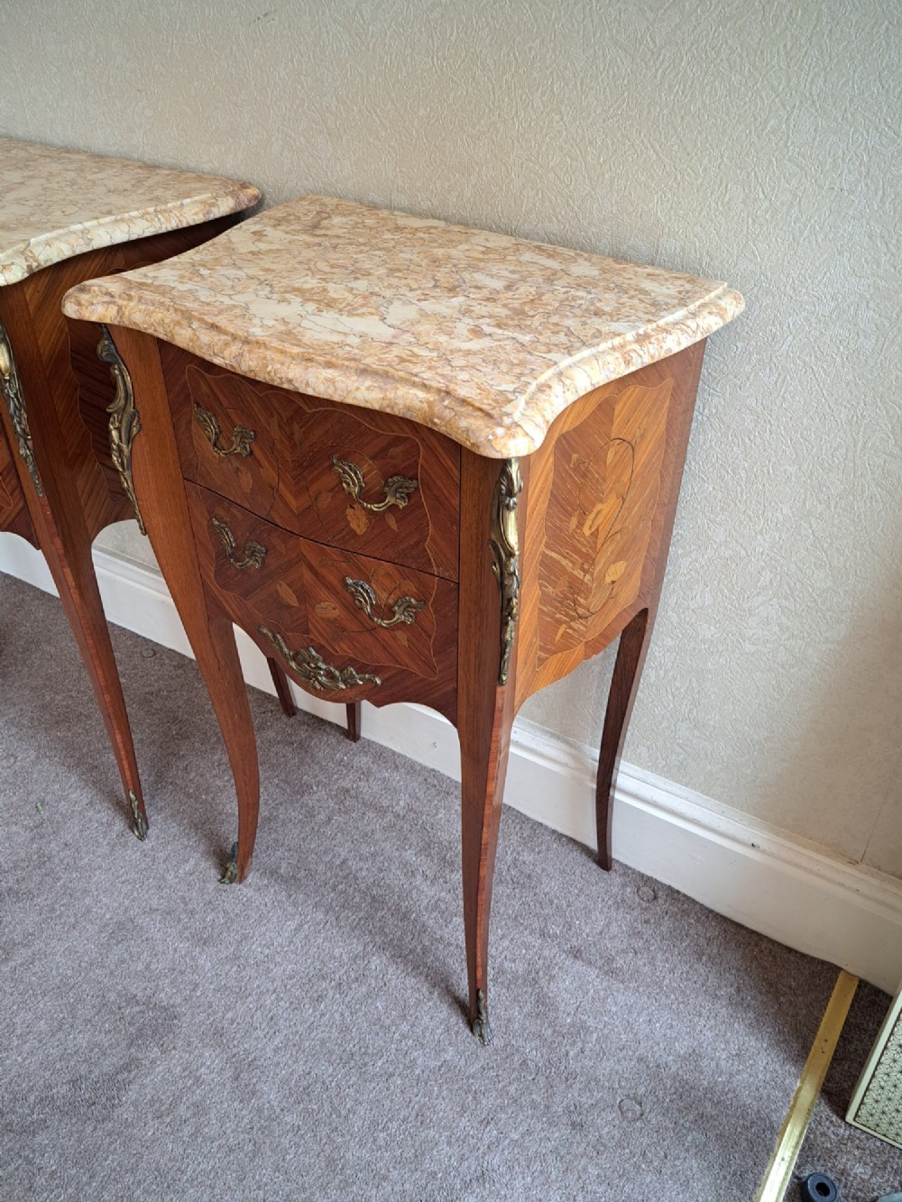 A pair of French style bedside tables featuring contoured beige marble tops, floral marquetry veneer drawers, brass handles, and sweeping cabriole legs. View IV