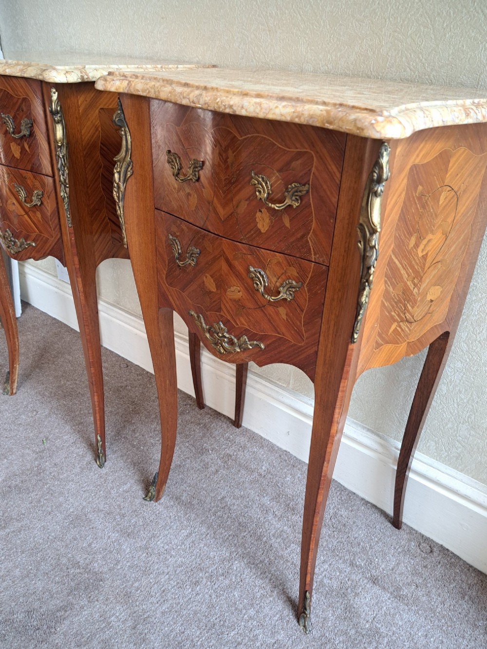 A pair of French style bedside tables featuring contoured beige marble tops, floral marquetry veneer drawers, brass handles, and sweeping cabriole legs. View V