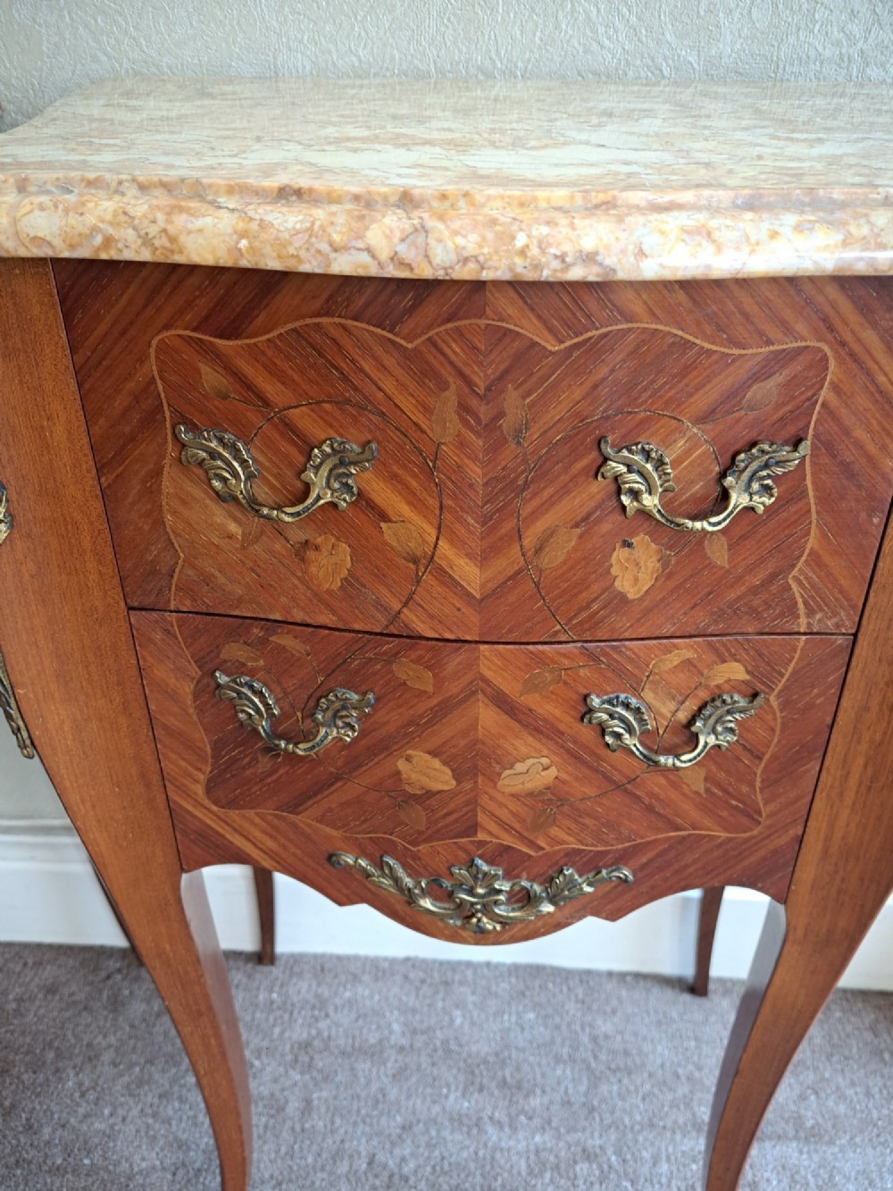 A pair of French style bedside tables featuring contoured beige marble tops, floral marquetry veneer drawers, brass handles, and sweeping cabriole legs. View VI