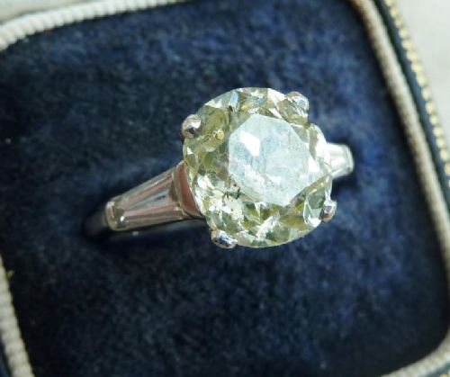fig 1. An Art Deco platinum solitaire ring set with a central round old cut diamond and flanked by stepped baguette cut diamonds on the shoulders.