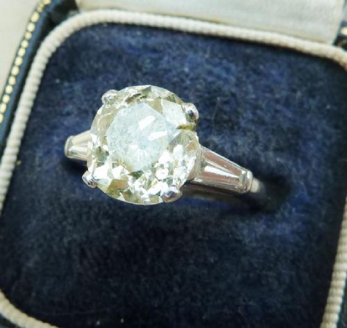 fig 2. An Art Deco platinum solitaire ring set with a central round old cut diamond and flanked by stepped baguette cut diamonds on the shoulders.