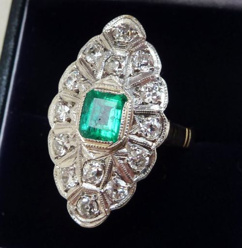 fig 1. An Edwardian marquise-shaped cluster ring featuring a central emerald-cut green emerald surrounded by old-cut diamonds set in white metal.