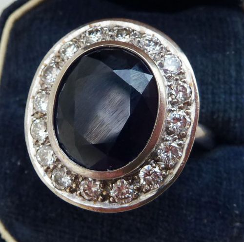 fig 1. An Art Deco style platinum cluster ring featuring a central oval facet-cut dark blue sapphire encircled by round brilliant diamonds.
