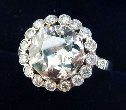 fig 1. An Art Deco platinum ring featuring a large round central diamond encircled by a halo of smaller round diamonds in a floral cluster design.