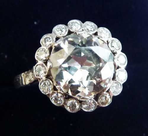 fig 2. An Art Deco platinum ring featuring a large round central diamond encircled by a halo of smaller round diamonds in a floral cluster design.