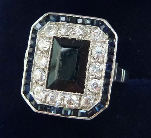 fig 1. An Art Deco platinum cluster ring featuring a central rectangular dark blue sapphire framed by round diamonds and an outer ring of calibre-cut sapphires.