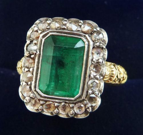 fig 1. A Georgian cluster ring featuring a central rectangular green emerald surrounded by a silver-set halo of rose-cut diamonds on an engraved yellow gold band.