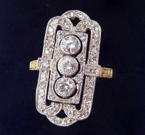fig 1. An Art Deco elongated rectangular plaque ring in 18ct yellow and white gold, set with three central round diamonds surrounded by a geometric filigree border of smaller diamonds.