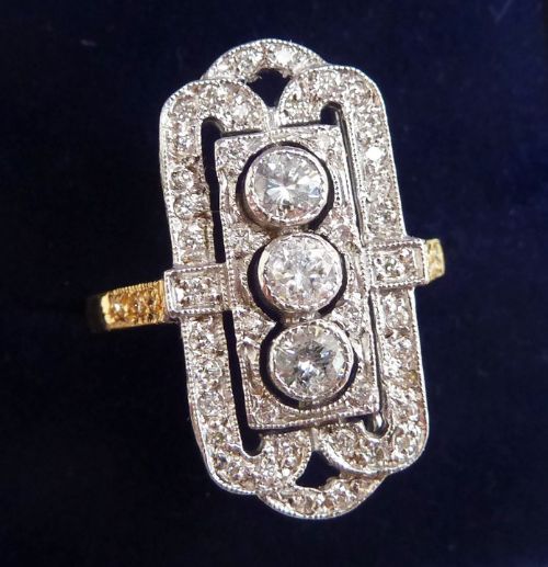 fig 2. An Art Deco elongated rectangular plaque ring in 18ct yellow and white gold, set with three central round diamonds surrounded by a geometric filigree border of smaller diamonds.