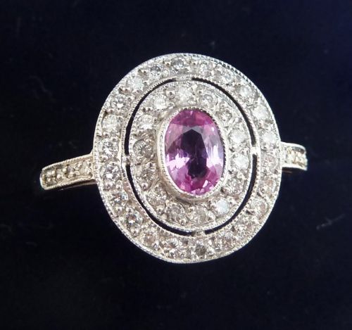 fig 1. An 18ct white gold Art Deco style cluster ring featuring a central oval pink sapphire enclosed by two oval halos of round diamonds with milgrain detailing.